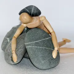 Drewniany ludzik leży przygnieciony kamieniami.