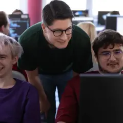 Studenci informatyki dyskutują o tym, ile zarabia informatyk po studiach, patrząc na ekrany komputerów.