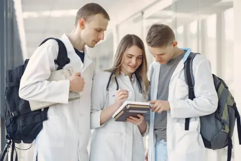 Trzech studentów medycyny w kitlach przegląda książki.