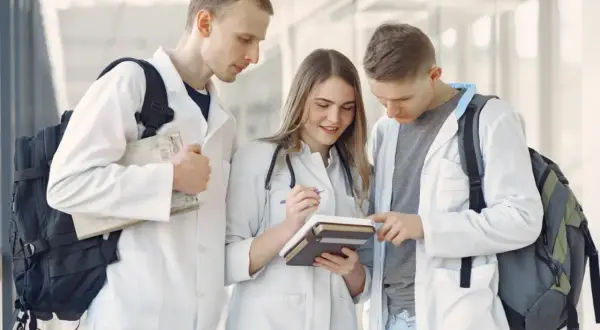 Trzech studentów medycyny w kitlach przegląda książki.
